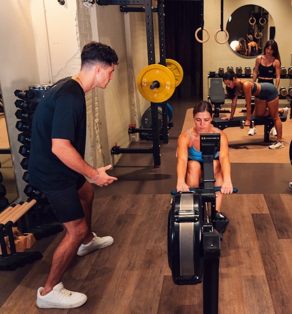 A women in a rowing machine being coach by a trainner